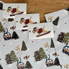 Load image into Gallery viewer, Close up of skiing soft coated wheaten terriers christmas wrapping paper and gift tags laydown on a wooden background