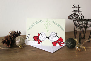 west highland white terriers under mistletoe wearing red ribbons.