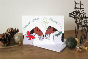 two wire fox terriers under mistletoe wearing holly and a red ribbon