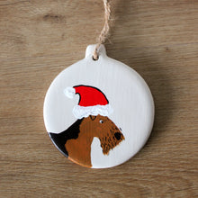 Load image into Gallery viewer, Ceramic Christmas decoration of a hand painted airedale wearing a Santas hat
