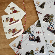 Set of Christmas-themed christmas wrapping paper gift tags with winter activities and trees on a wooden surface.