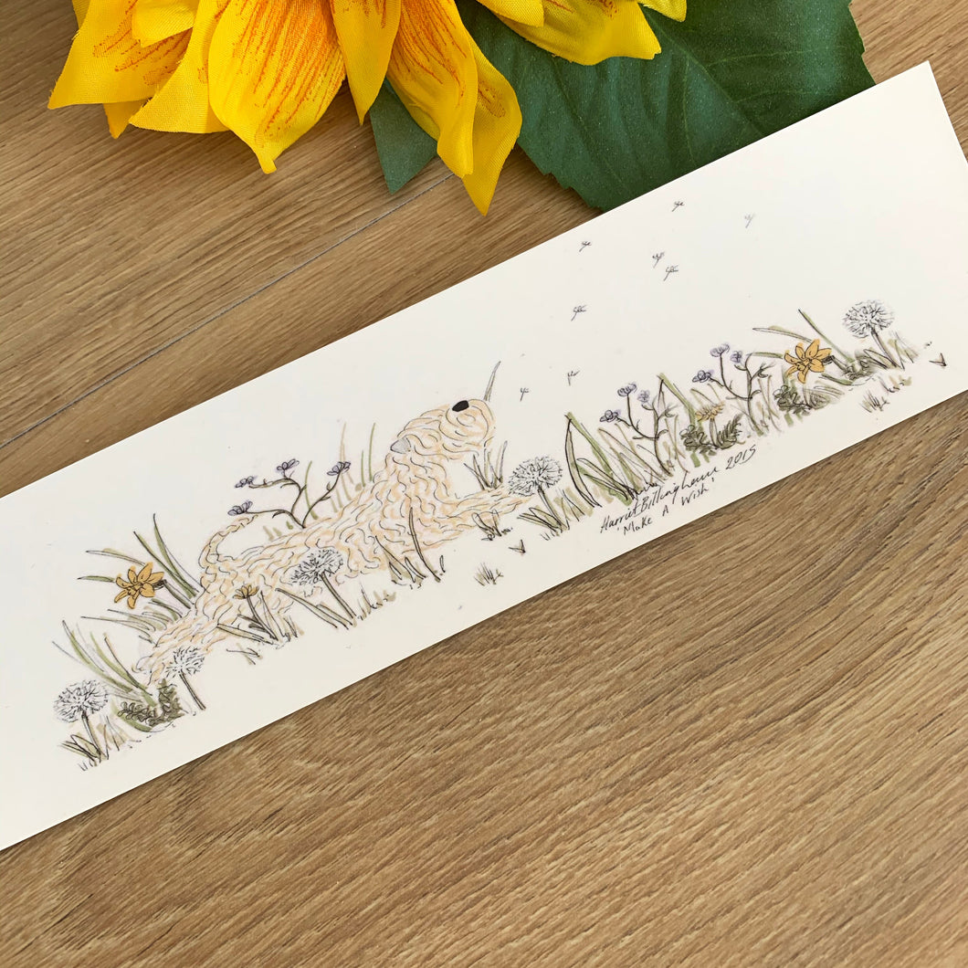 Decorative bookmark with a soft coated wheaten terrier on with nature-themed design on a wooden surface with a sunflower.