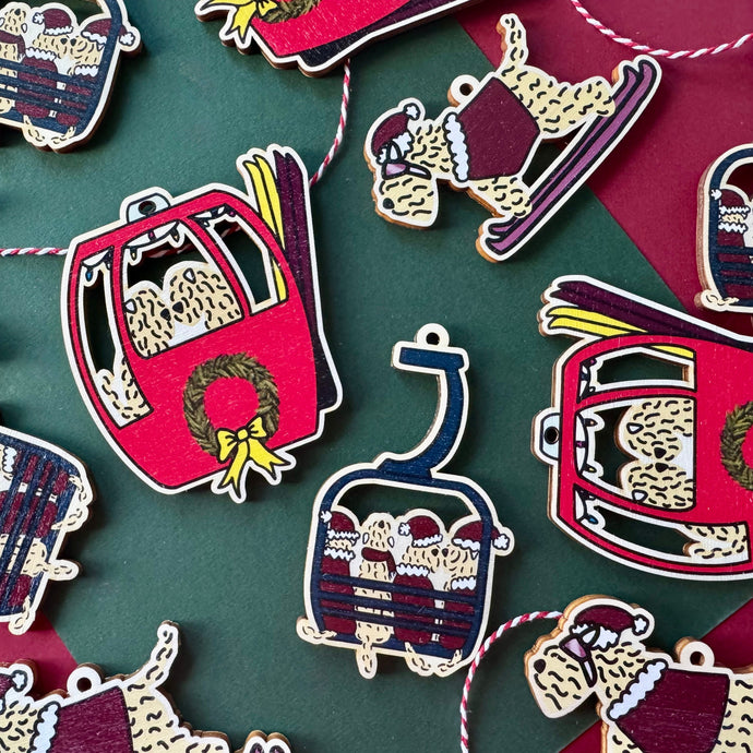 Decorative Wheaten Christmas ornaments on a green and red background. Each decoration is a ski theme.