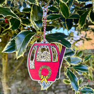 Decorative Christmas ornament shaped like a red gondola with a wreath and bow, hanging from green leaves.