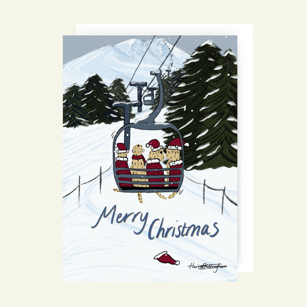 Greeting card with a ski lift and Wheatens wearing Santa hats against a snowy mountain background.