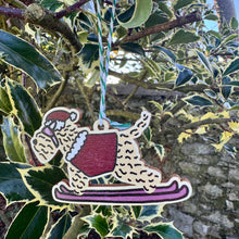 Load image into Gallery viewer, Decorative ornament of a dog skiing hanging from a tree branch.

