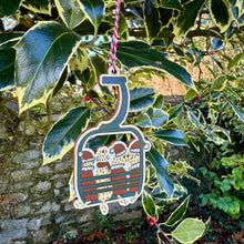 Load image into Gallery viewer, Decorative ornament shaped like a ski lift with a Santa Claus design hanging from holly leaves.
