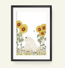 Load image into Gallery viewer, A framed art print featuring a whimsical illustration of a soft coated wheaten terrier among yellow sunflowers and green grass, displayed on a light beige wall.

