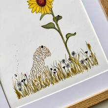 Load image into Gallery viewer, A framed art print featuring a whimsical illustration of a small dog sitting in a field beneath a large yellow sunflower, shown with a white mat and light wood frame.
