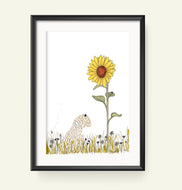 A framed art print featuring a whimsical illustration of a soft coated wheaten terrier in a field beneath a large sunflower, displayed on a light cream background.